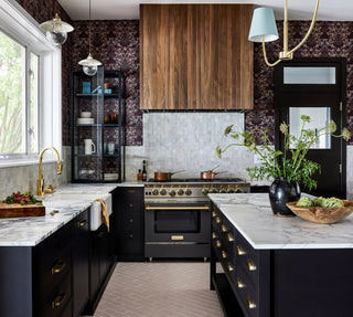 A kitchen with a bold yet functional design with dark tones, wallpaper, a wood hood, marble countertops, and a chef's range.