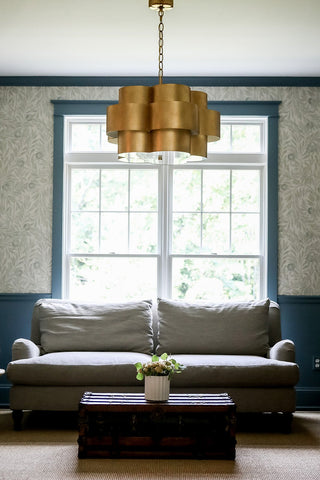 Front view of a living room with a plush couch, blue wainscoting, vintage table, and a statement ceiling light fixture.