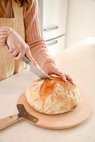A hand cutting into a freshly based loaf of bread.