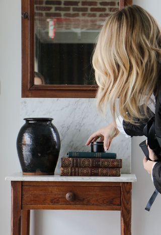 Antique decor - wooden mirror and accent side table with a glossy terracotta vase and antique books.