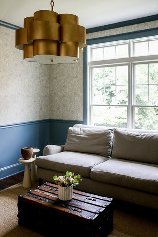 A bold and rustic living room style with vintage trunk table, blue wainscoting, and large handing lamp.