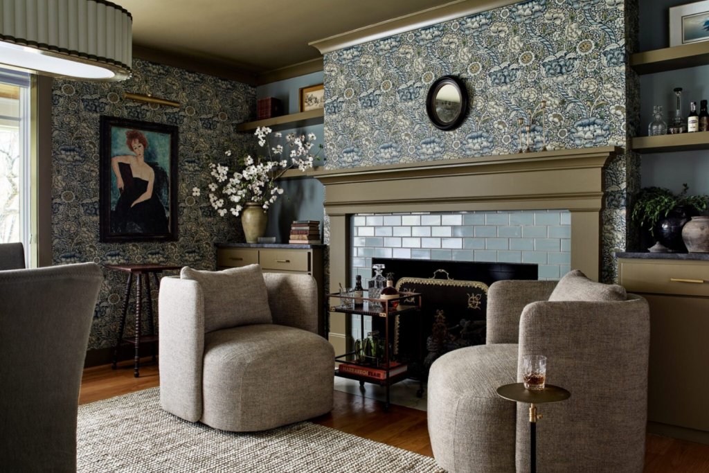 Interior design return on investment: moody living room with bold Morris-style floral wallpaper, olive green built-ins, fireplace with sage subway tile surround, and curved linen swivel chairs — designed by Details and Design, Annapolis Maryland.