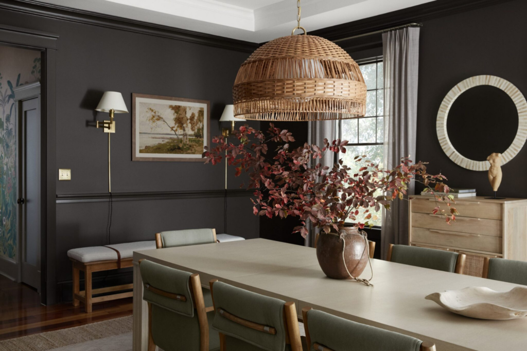 Interior design return on investment: dramatic dark-walled dining room with large wicker pendant light, sage green dining chairs, natural wood dresser, and richly layered art and textiles — designed by Details and Design, Annapolis Maryland.